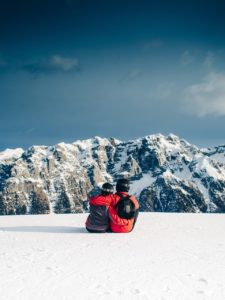 Couple sitting in snow looking at mountains together